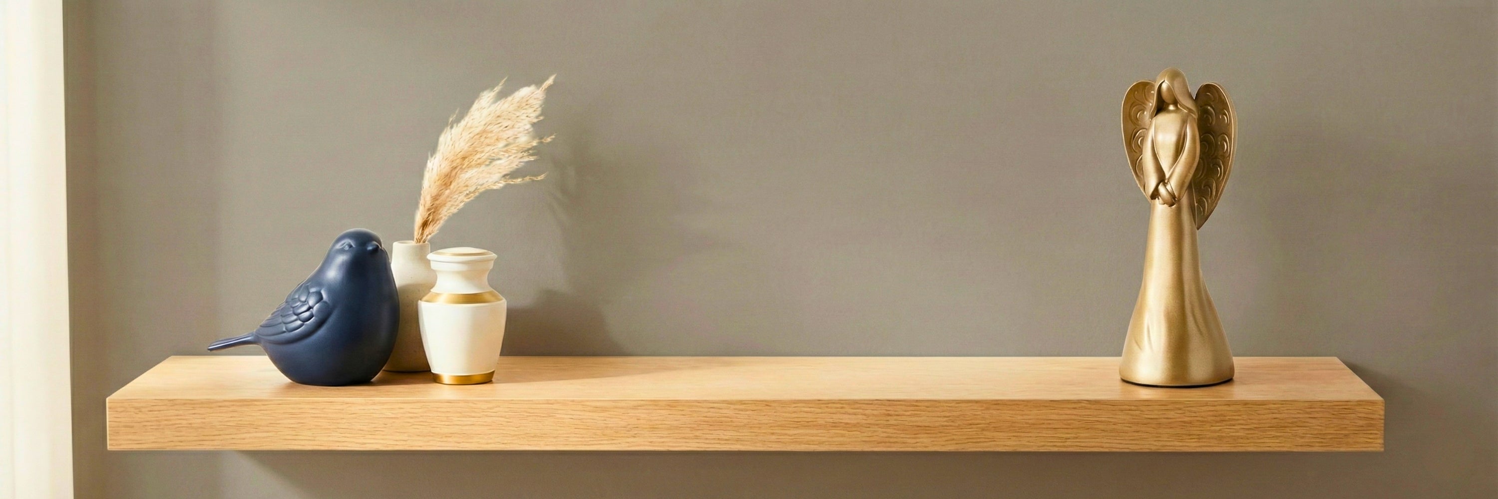 Memorial keepsake collection with blue bird figurine, miniature white and gold urn, and gold angel statue on floating wood shelf — Magnolia Memorial Marketplace